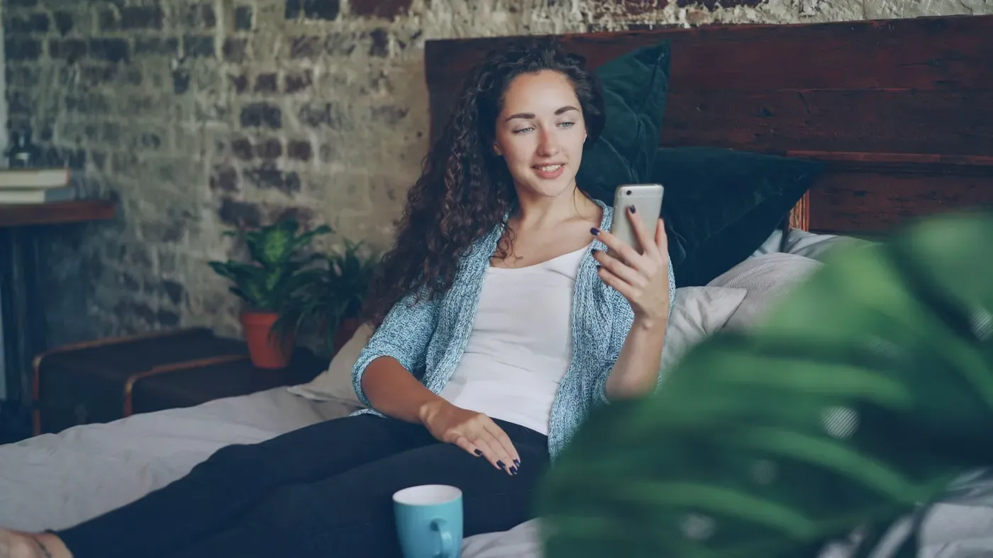 Junge Frau liegt entspannt mit ihrem Smartphone im Bett