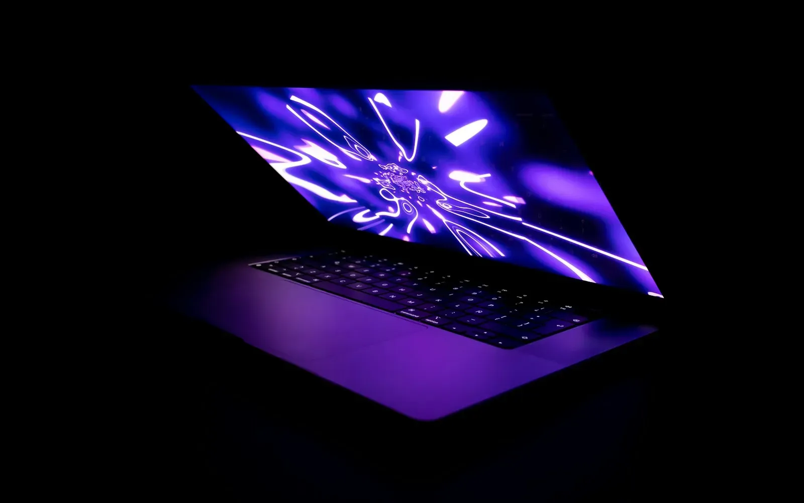 Aufgeklappter Laptop mit violett leuchtendem Bildschirm in einem dunklen Raum
