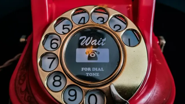 Rotes Wählscheibentelefon mit goldener Wählscheibe vor dunklem Hintergrund – Telefonsex oder Sexchat im Vergleich